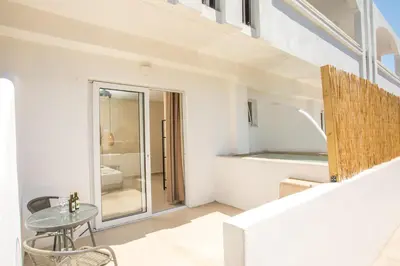 a white apartment with a table and a bathroom at Atma Beach Rooms & Suites in Faliraki