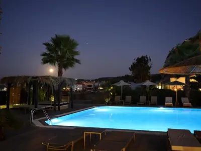 a swimming pool at night with a palm tree and umbrellas at Ixia Dream hotel - Adults only in Ixia