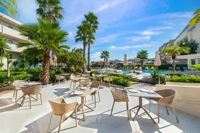a patio at the resort with tables and chairs and palm trees at Ixia Dream hotel - Adults only in Ixia