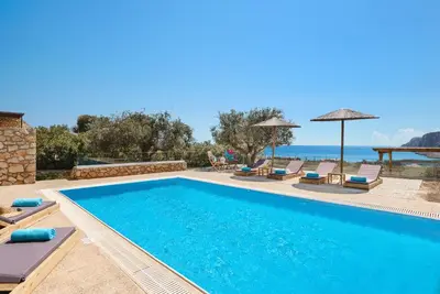 a swimming pool with chairs and the ocean in the background at Blue Line Villa Lindos in Líndos