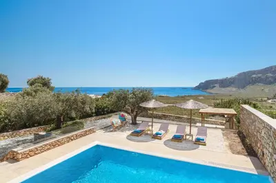 a swimming pool with chairs and umbrellas and the ocean at Blue Line Villa Lindos in Líndos