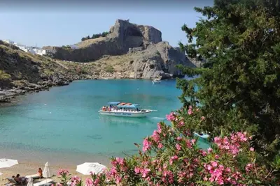 a boat in a body of water with a mountain at Blue Line Villa Lindos in Líndos