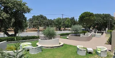 a park with white chairs and tables and trees at Santa Helena Hotel in Ialyssos