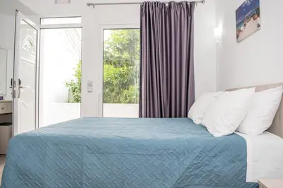 a bedroom with a bed with a blue blanket and a window at Red Hibiscus Stegna in Archangelos