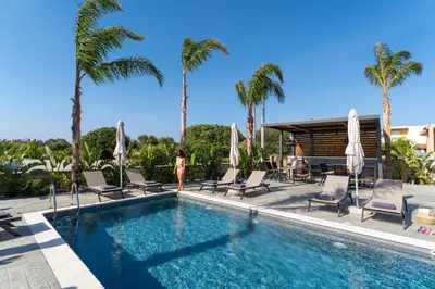 a woman standing next to a swimming pool with palm trees at Palmeral Luxury Suites in Rhodes Town