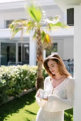 a woman holding a cup of coffee in front of a house at M Mansion in Pefki Rhodes