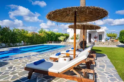 a group of chairs and an umbrella next to a swimming pool at Villa Palmeras in Soroni