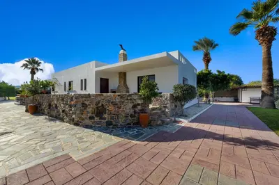 a house with a stone wall and palm trees at Villa Palmeras in Soroni