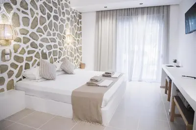 a white bedroom with a bed and a stone wall at Ladiko Inn Hotel Faliraki -Anthony Quinn Bay in Faliraki