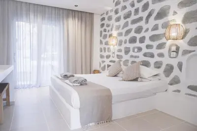a white bedroom with a bed and a stone wall at Ladiko Inn Hotel Faliraki -Anthony Quinn Bay in Faliraki