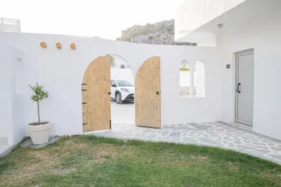 a white house with wooden doors and a car parked at Ladiko Inn Hotel Faliraki -Anthony Quinn Bay in Faliraki