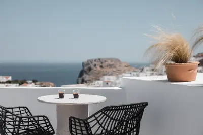 a table and chairs on a balcony with a view of the ocean at Noema Lindos - Agapitos Apartment in Líndos