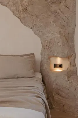 a bed with a light on the side of a stone wall at Noema Lindos - Agapitos Apartment in Líndos
