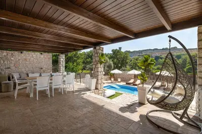 a patio with a table and chairs and a pool at Adonis Villa in nature in Ixia
