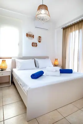 a white bedroom with a large white bed with blue pillows at Memi Beach front Villa in Kiotari