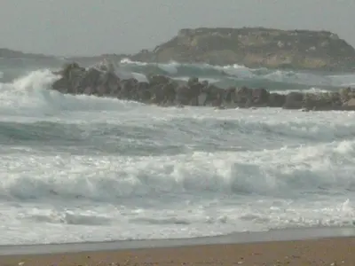 a beach with waves and a rocky island in the ocean at Ammos stegna in Archangelos
