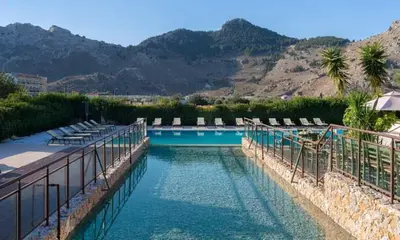 a swimming pool with chairs and mountains in the background at Anavadia Hotel-All Inclusive in Kolimbia