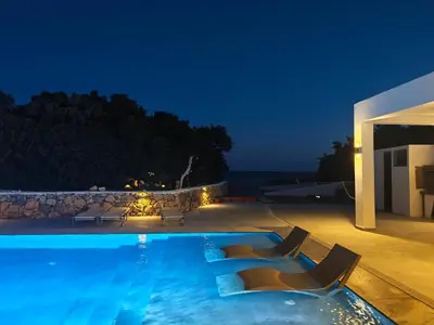 a swimming pool at night with chairs around it at Cathrin Beachfront Villa in Plimmiri