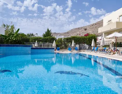a large blue swimming pool with chairs and a building at Lindos Athena in Líndos