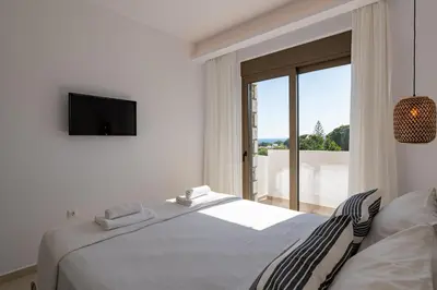 a white bedroom with a bed and a window at VILLA IRIS in PEFKOS, PINE VILLAS in Pefki Rhodes