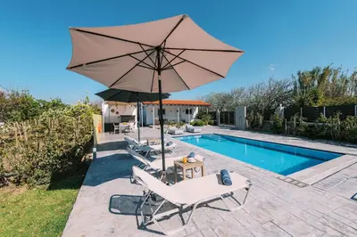 a pool with a umbrella and two chairs and a table and a pool at Reni Garden House in Afantou