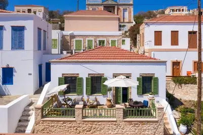 a white house with green shutters and chairs and an umbrella at Muse Clio in Halki