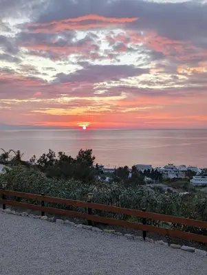 a sunset over the ocean with a wooden fence at KIRA'S RESIDENCE PANORAMIC VIEW in Archangelos