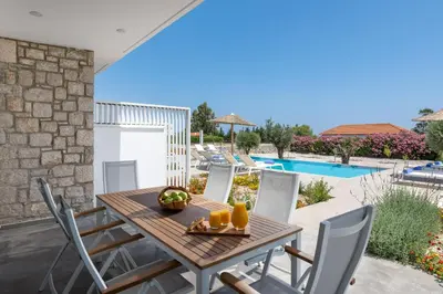 a patio with a wooden table and chairs and a pool at Gennadi Harmony Suites - 200 m from the sea in Gennadi