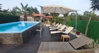 a deck with chairs and an umbrella next to a pool at Nila's Villa in Koskinou
