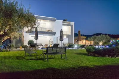 a house with a lawn with two benches and umbrellas at Mika Villa in Afantou