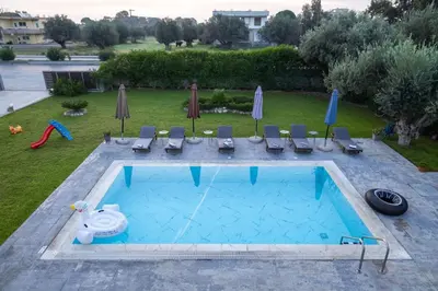 a swimming pool with chairs and umbrellas in a yard at Mika Villa in Afantou
