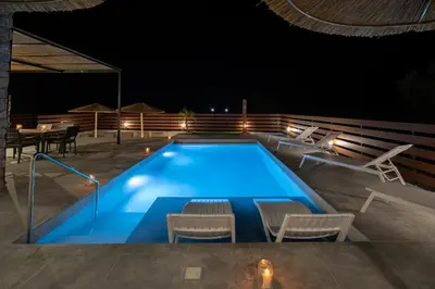 a swimming pool at night with chairs and a table at Terra Secreta Luxury Villas in Lardos