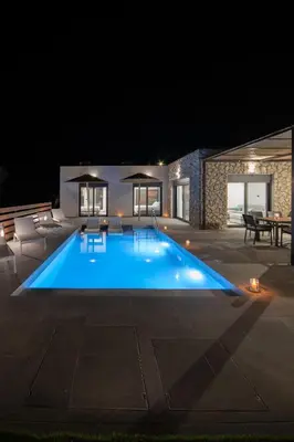a swimming pool at night with tables and chairs at Terra Secreta Luxury Villas in Lardos