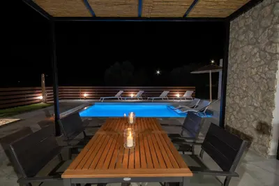 a wooden table and chairs next to a swimming pool at night at Terra Secreta Luxury Villas in Lardos
