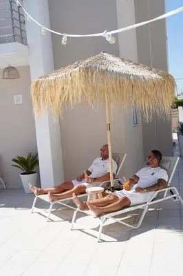 two men sitting on chairs under a straw umbrella at Villa Pastida - Private Pool & Jacuzzi & Central place in Pastida