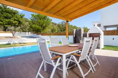 a wooden table and chairs on a patio with a pool at Rhodian Dunes Villas with Private Pool in Kiotari