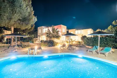 a swimming pool with chairs and umbrellas at night at CrossRhodes Villas in Pefki Rhodes