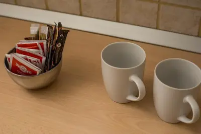 two white cups sitting on a table with a bowl of scissors at Economisa Apartments in Ialyssos