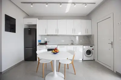 a white kitchen with a white table and chairs at The Azure Blue Apt Faliraki in Faliraki