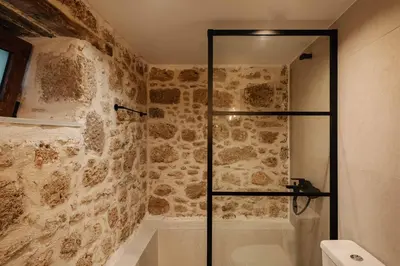a bathroom with a walk in shower next to a stone wall at La casa dell'arch in Haraki
