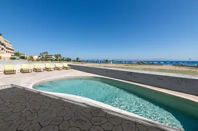 a swimming pool next to a beach with chairs at White&Blue Beachfront Luxury Suite in Ialyssos