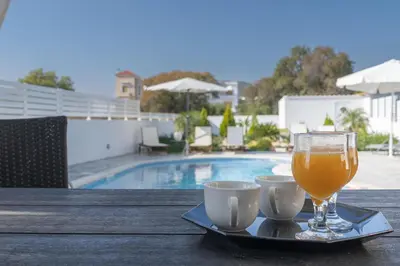 a glass of orange juice and two cups on a table next to a pool at Dama Dama Villas in Gennadi