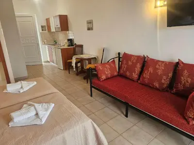 a living room with a red couch and a kitchen at Apollonio Rooms Faliraki Rhodes in Faliraki