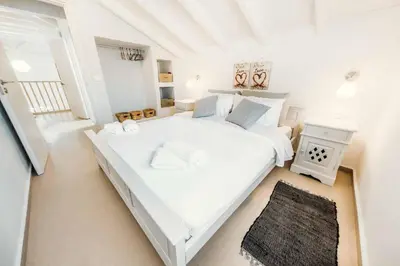 a white bedroom with a large white bed and a rug at Ammos Beach House in Kiotari