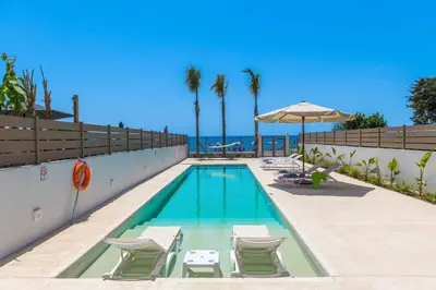 a swimming pool with chairs and an umbrella and the ocean at Ammos Beach House in Kiotari