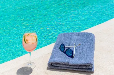 a drink and sunglasses next to a swimming pool at Ammos Beach House in Kiotari