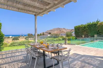 a wooden table and chairs on a patio with a pool at Villa Krini Myth in vlicha
