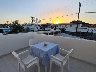 a table and chairs on a balcony with the sunset at Stonegarden Studios in Faliraki