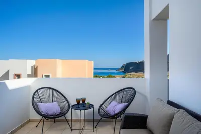 a balcony with two chairs and a table with purple pillows at Adore Lindos Villa in Líndos