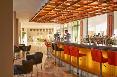 a man standing behind a bar with red chairs at Lindos Bay Hotel in vlicha